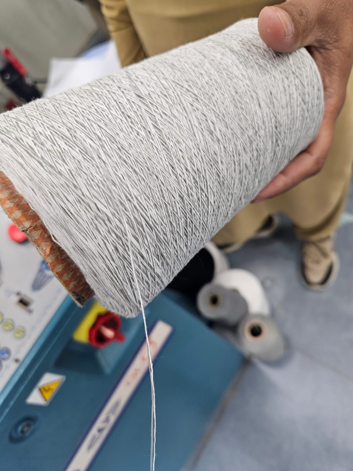 Grey yarn cone inspected on the production floor, where control begins at yarn sourcing.